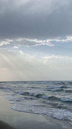 the sun shines through the clouds over the water at the beach on a cloudy day