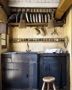 an old fashioned kitchen with wooden stools and hats hanging on the wall above it