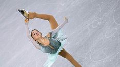 a female figure skating on the ice in a dress and holding a gold shoe with her right hand