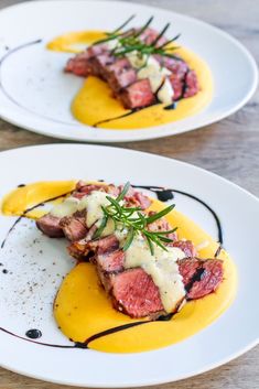 two white plates topped with meat covered in sauce and garnished with green herbs