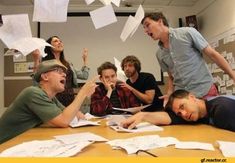 a group of people sitting around a table with papers flying in the air over them