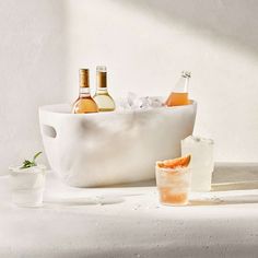 bottles and glasses sitting on a table with ice in the tub next to each other