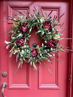 a red door with a wreath hanging on it's side and flowers in the middle