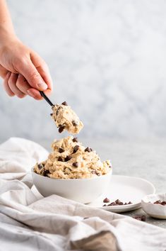 a person scooping chocolate chip ice cream out of a white bowl on a plate