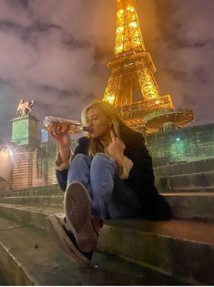 a woman sitting on steps drinking from a wine glass in front of the eiffel tower