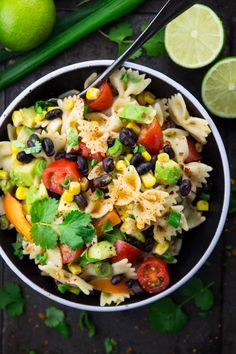 a bowl filled with pasta salad next to limes