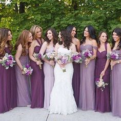 a group of women standing next to each other wearing purple dresses and holding bouquets