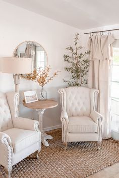 a white living room with two chairs and a table in front of a mirror on the wall