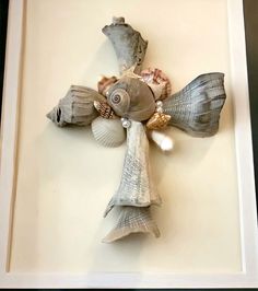 a cross made out of seashells in a white frame on a table top