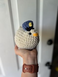 a hand holding a small crocheted bird with a hat on it's head