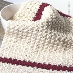 a crocheted blanket sitting on top of a table next to a white bowl