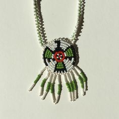 Indian beaded necklace with eagle pendant in green, red, white  and black. Pendant depicts an eagle. Total length of chain is 22.5" (all the way around) and from mid-way of chain to end of pendant is 14 inches. Pendant is 1.5 inches in diameter. Pendant has green and white beaded fringe. White Beaded Round Pendant Necklaces, Southwestern Green Necklace With Large Pendant, Southwestern Style Green Necklace With Large Pendant, Southwestern Style White Beaded Necklace As Gift, Green Southwestern Beaded Necklace Gift, Green Southwestern Style Beaded Necklace As Gift, Green Southwestern Style Beaded Necklace For Gift, Southwestern Style Green Beaded Necklace For Gift, Southwestern Style Green Beaded Necklace Gift