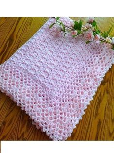 a pink crocheted blanket sitting on top of a wooden floor next to flowers