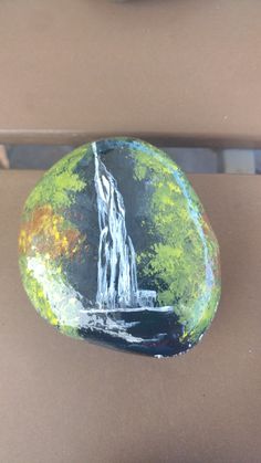 a rock with a waterfall painted on it sitting next to a bowl filled with fruit