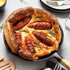 a cast iron skillet with sausages and cheese in it on a table next to utensils