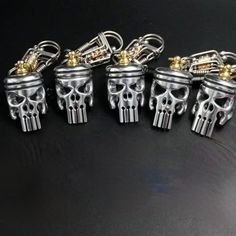 five silver skull key chains on a black surface with gold accents and metal fittings