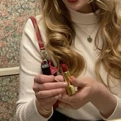 a woman with long blonde hair is holding a lipstick in her hand and looking at the camera