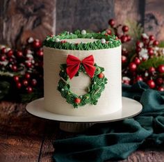 a decorated christmas cake sitting on top of a wooden table next to holly wreaths