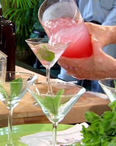 someone pouring drinks into martini glasses on a table