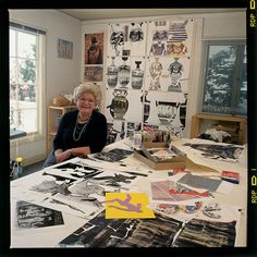 a woman sitting at a table covered in pictures and papers with scissors on top of it