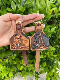 a hand holding two small leather keychains with horses on them