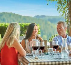 three people sitting at a table with wine glasses in front of them, talking and laughing