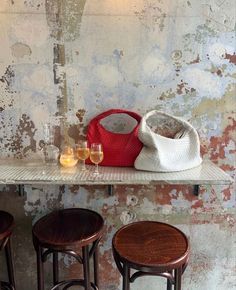 three wooden stools and two wine glasses on a shelf in front of a wall with peeling paint