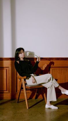 a woman is sitting on a chair holding a paper in one hand and looking at the other