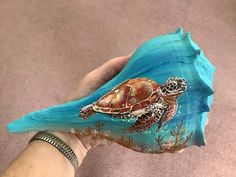 a sea turtle painted on a rock with blue water and corals is held by a woman's hand