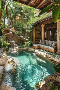 an outdoor swimming pool surrounded by greenery and stone patio furniture, with a waterfall in the center