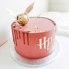 a pink cake with white frosting and a gold decoration on top that says hp