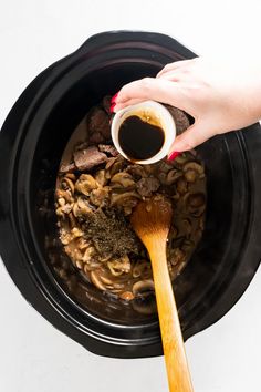 someone is stirring up some food in the crock pot with a wooden spoon and sauce