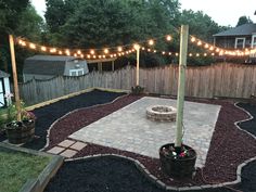 an outdoor patio with lights strung over the fire pit and seating area in the back yard