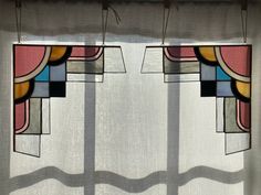 two stained glass panels hanging from the side of a window in front of a curtain