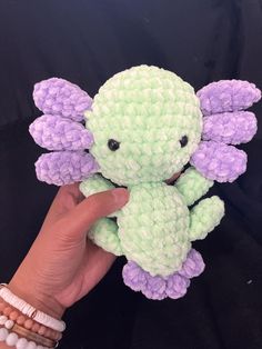 a hand holding a small green and purple stuffed animal