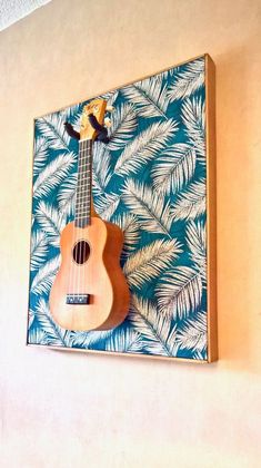 a wooden ukulele hanging on the wall next to a blue and white palm leaf pattern