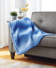 a gray couch with a blue blanket on top of it next to a white rug