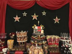 a table topped with lots of desserts and candies next to a red curtain