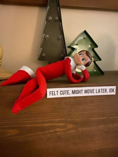 an elf is laying on top of a desk next to a christmas tree and a sign