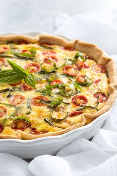 a quiche with tomatoes and basil in a pie dish on a white tablecloth