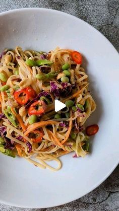 a white bowl filled with pasta and vegetables on top of a table next to a fork