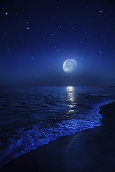 the moon is shining brightly over the water at night on the beach with waves crashing in front of it