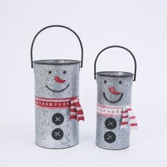 two tin canisters with faces painted on them, one has a red bow and the other is a snowman