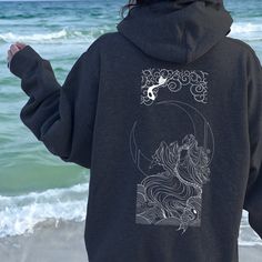 a person standing on the beach with their back to the camera, wearing a black hoodie