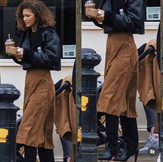 the woman is wearing an apron and holding a drink while walking down the street with her hand in her pocket