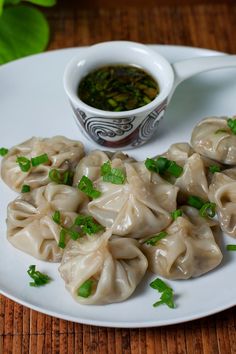 some dumplings are sitting on a white plate next to a small bowl of dipping sauce