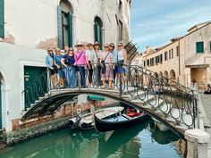 a group of people standing on a bridge next to a boat in the water near buildings