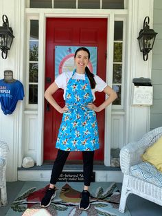 a woman standing in front of a red door with her hands on her hips wearing an apron