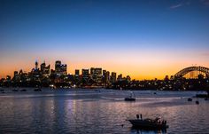 boats are in the water near a city at sunset or dawn, with lights on