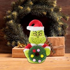 a green stuffed animal wearing a santa hat next to a christmas wreath on a table